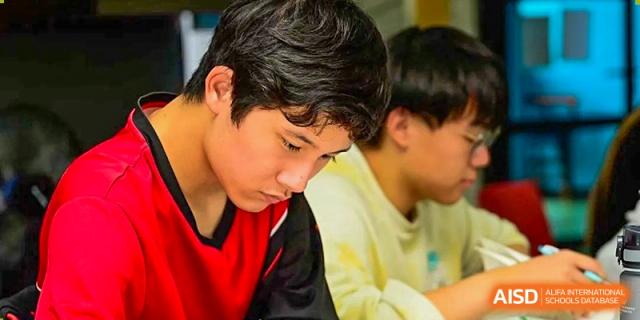 Two students sit close together and focus intently on their individual schoolwork during a quiet and productive study session at Beijing City International School.
