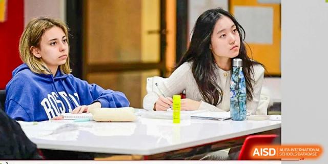 A student sits at a white table and looks thoughtfully into the distance while participating in a classroom discussion or lecture at Beijing City International School.