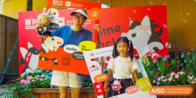 A young girl and a staff member pose with fun, colorful cardboard photo frames during a festive welcome back event held on the campus of Beijing City International School.