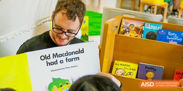 An educator smiles while reading the classic book Old Macdonald Had a Farm to a young, engaged student in a colorful and welcoming school library at Beijing City International School.