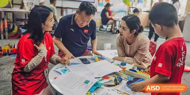 Three adults gather around a circular table in a bright room to review and discuss several educational documents and colorful charts together at Beijing City International School.
