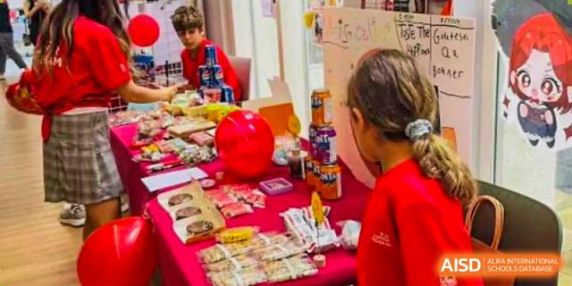 Students and staff gather around a long table covered in various snacks and drinks during a festive community event or school fundraiser held at Beijing City International School.