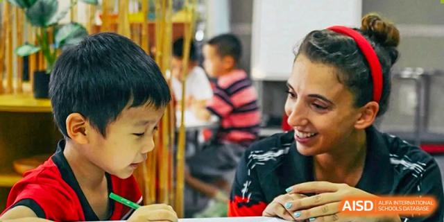An educator shares a joyful moment with a young student while assisting them with a hands-on learning activity in a classroom filled with natural light at Beijing City International School.