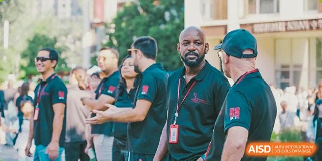 A diverse group of faculty members in matching dark polo shirts gathers outdoors for a meeting or social event on the campus of Beijing City International School.