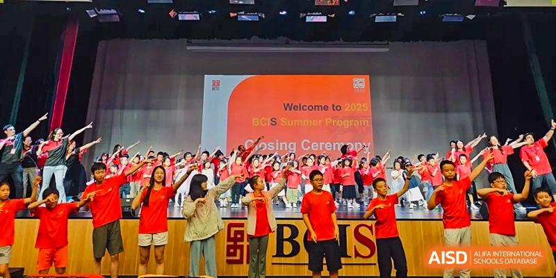 A large choir of students in red shirts performs on a stage during the 2025 summer program closing ceremony held at Beijing City International School.