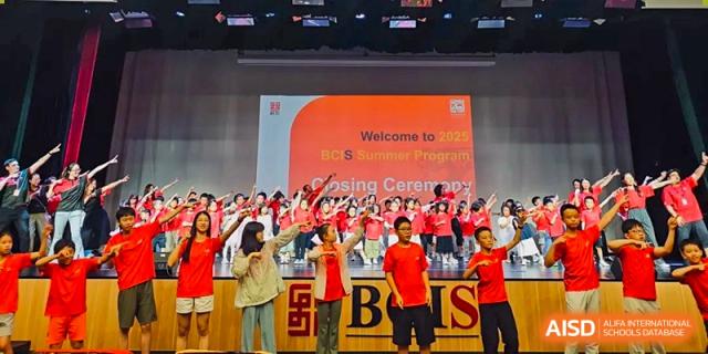 A large choir of students in red shirts performs on a stage during the 2025 summer program closing ceremony held at Beijing City International School.