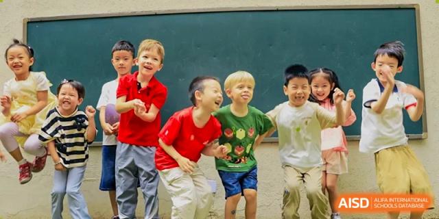 A diverse group of young children stands in front of a chalkboard laughing and showing joyful expressions during a playful moment between lessons at Beijing City International School.