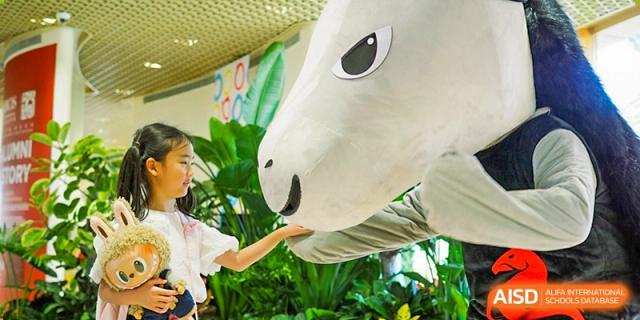 A young student gently reaches out to touch the nose of a large, white inflatable mascot character during a fun and interactive campus event at Beijing City International School.