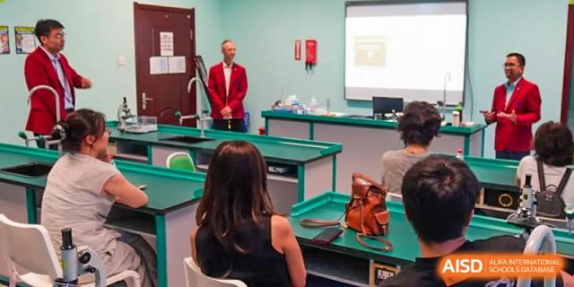 A male teacher in a red blazer presents in a modern science laboratory to seated parents at the Canadian International School of Shenyang.