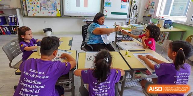 A teacher assists a student with a seated desk activity in a bright, decorated classroom at the Canadian International School of Shenyang.