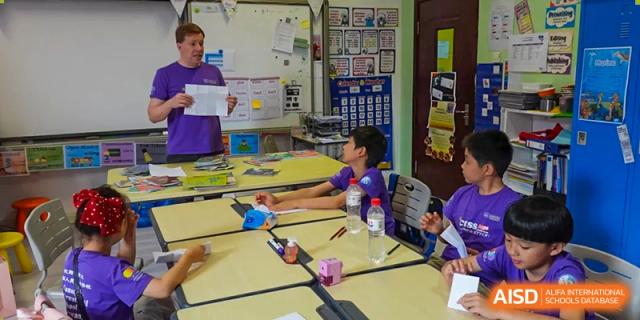 A teacher in a purple shirt interacts with a student seated at a desk during a classroom lesson at the Canadian International School of Shenyang.