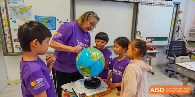 A teacher and several young students gather around a desk to examine a colorful world globe at the Canadian International School of Shenyang.