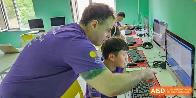A teacher in a purple shirt assists a student working on a computer during an IT lesson at the Canadian International School of Shenyang.