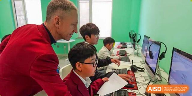 A student in a red school blazer works diligently at a computer station in a modern lab at the Canadian International School of Shenyang.