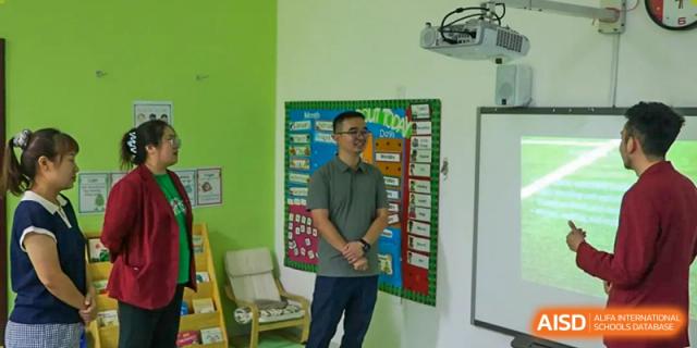 A staff member stands and smiles in front of a colorful "What’s the Weather Today" board at the Canadian International School of Shenyang.