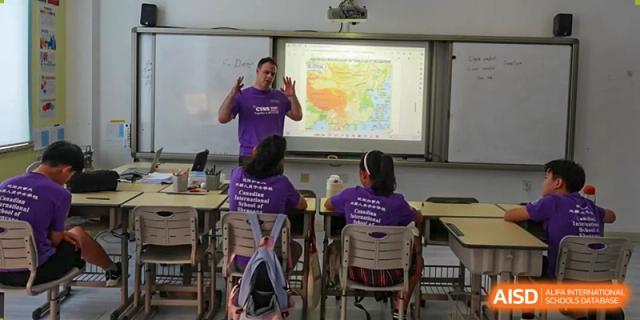 Students in purple school shirts watch an interactive presentation on a large screen in a classroom at the Canadian International School of Shenyang.