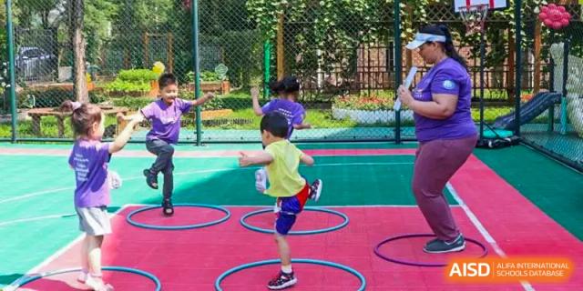 Children in colorful sportswear participate in a balance and coordination activity using hula hoops on an outdoor playground at the Canadian International School of Shenyang.