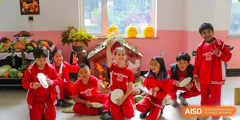 Students in red uniforms smile and raise their hands during an interactive indoor lesson in a bright, decorated classroom at the Canadian International School of Shenyang.