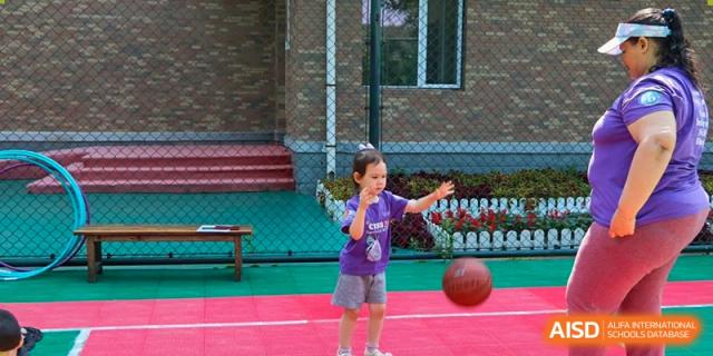 A young girl in a purple shirt practices dribbling a basketball on a red and green outdoor sports court during recess at the Canadian International School of Shenyang.