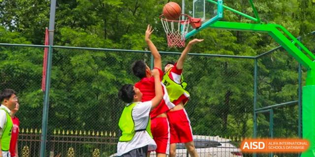 Young students in athletic gear practice their shooting skills on an outdoor basketball court during a physical education class at the Canadian International School of Shenyang.