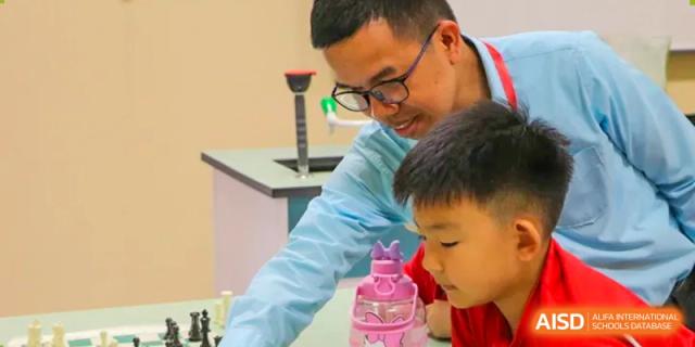A teacher assists a young student with a hands-on classroom project involving colorful materials at the Canadian International School of Shenyang.