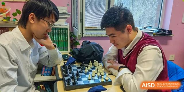 Two male students concentrate on a strategic game of chess during an indoor extracurricular activity at the Canadian International School of Shenyang.