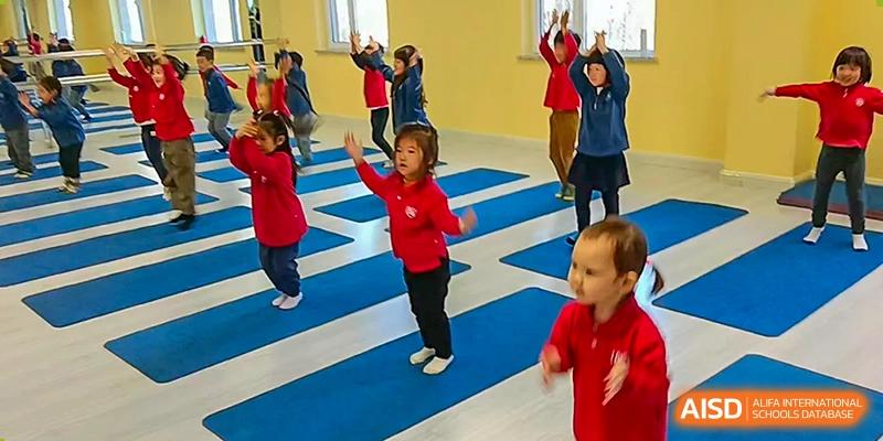 Young children in red uniforms participate in a group exercise or dance routine on blue mats at the Canadian International School of Shenyang.