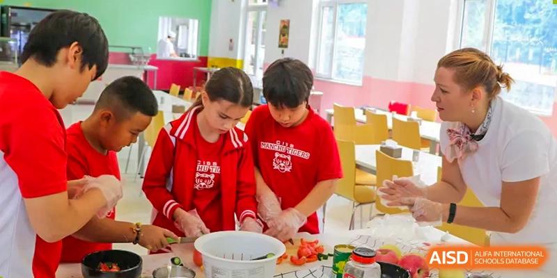 Two students in red school uniforms work together on a food preparation or cooking project at the Canadian International School of Shenyang.