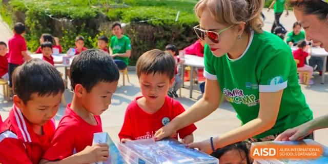 A teacher in a green shirt helps students with an outdoor learning activity on a sunny day at the Canadian International School of Shenyang.