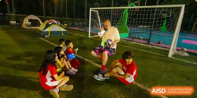 Students sit on an outdoor field at night listening to a staff member during a camping or team event at the Canadian International School of Shenyang.