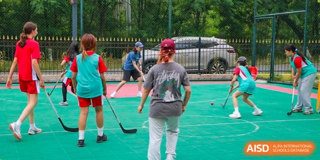 Students practice their field hockey skills on an outdoor green sports court during a physical education lesson at the Canadian International School of Shenyang.
