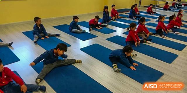 Young students sit on blue mats in a bright classroom while practicing stretching exercises at the Canadian International School of Shenyang.