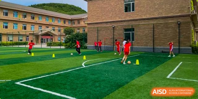 Students in red sports uniforms practice soccer drills on an outdoor green turf field at the Canadian International School of Shenyang.