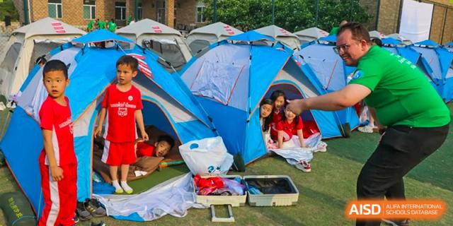 Students smile and pose from inside blue and grey camping tents set up on the school lawn for an outdoor event at the Canadian International School of Shenyang.