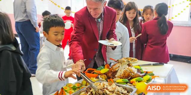 A teacher in a red blazer assists at a formal buffet station featuring a large roasted turkey at the Canadian International School of Shenyang.