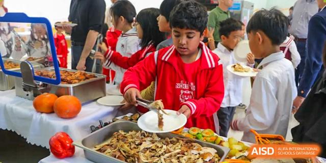 A young student in a red jacket uses tongs to serve themselves from a variety of prepared dishes at the Canadian International School of Shenyang.
