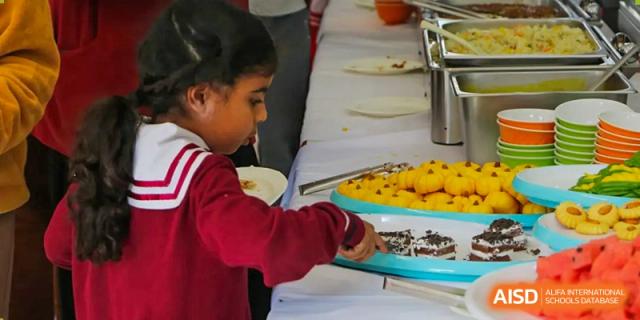 A young student in a red school uniform carefully selects a treat from a colorful dessert tray at a buffet event at the Canadian International School of Shenyang.