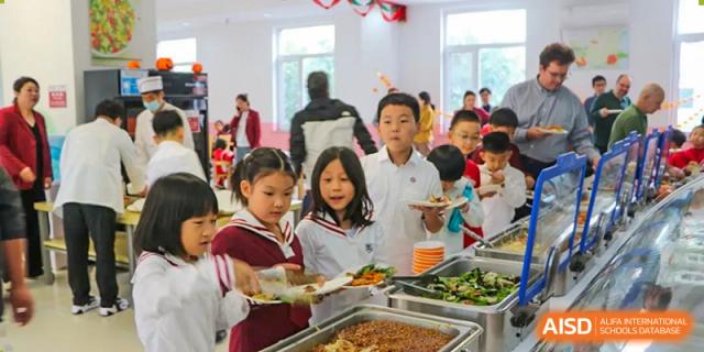 Students in school uniforms line up to choose from a selection of healthy cooked vegetables and grains at the Canadian International School of Shenyang.