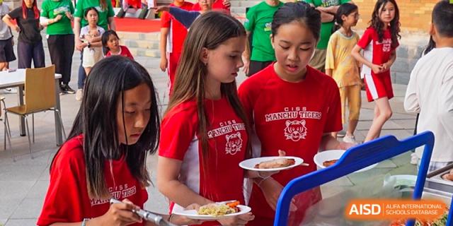 Students wearing red "Manchu Tiger" school shirts wait in line with their plates for a meal during an outdoor event at the Canadian International School of Shenyang.