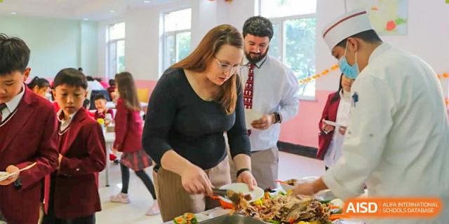 Two staff members work together to serve fresh food from a large catering tray during a school luncheon event at the Canadian International School of Shenyang.