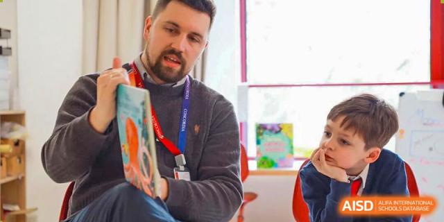 A male teacher with a beard reading a book to students, demonstrating engaging classroom instruction and literacy focus at Concordia International School Ningbo.