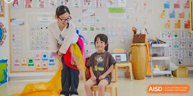 A female teacher smiling while engaging with two young students seated in a brightly lit classroom, focusing on early childhood education at Concordia International School Ningbo.