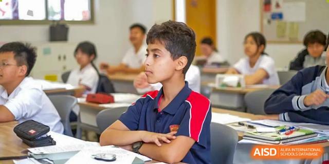 A male student in a school uniform sitting at a desk, looking attentively at the teacher during a focused learning session at Concordia International School Ningbo.