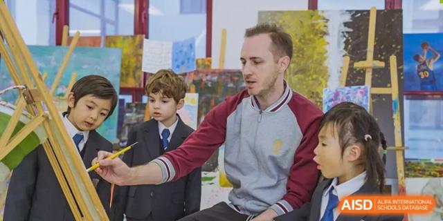 A male teacher sitting with young students in uniform, engaging in a one-on-one conversation during a casual, focused learning moment at Concordia International School Ningbo.