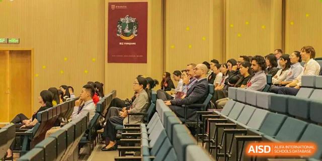 An audience of adults, including men in suits, sitting attentively in an auditorium or hall during a formal school event at Concordia International School Ningbo.