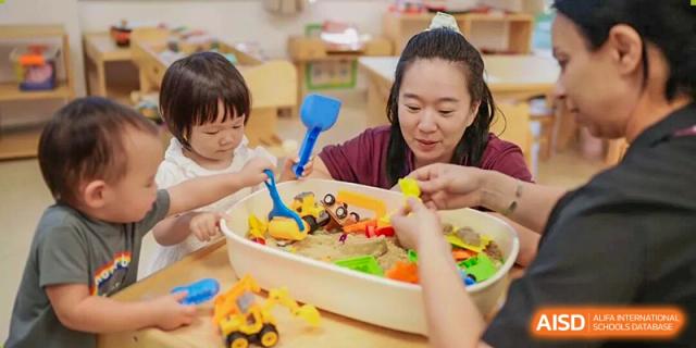 A teacher and young children playing together with sand, toys, and small plastic tools in a brightly lit classroom or learning center at Concordia International School Ningbo.