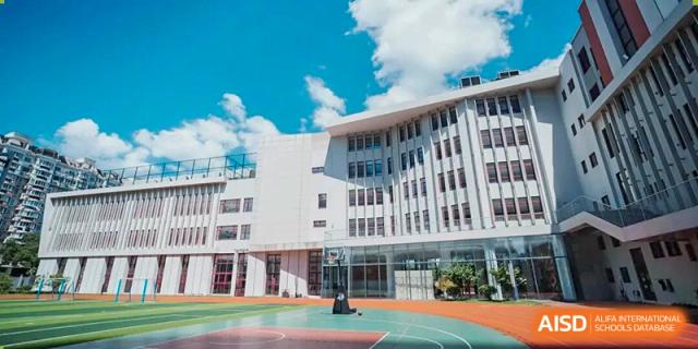 A modern, bright school building with large windows and a sports court in the foreground, showing the campus facilities of Concordia International School Ningbo.
