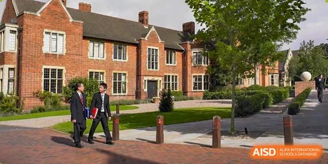 An adult walking in front of a traditional, red-brick school building with a manicured lawn, representing the architecture of Concordia International School Ningbo.