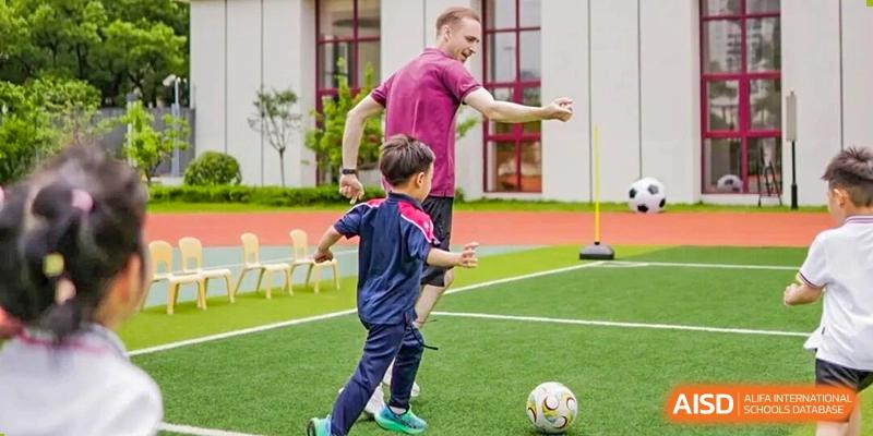 A coach in a pink shirt instructing a young student on a green field with a soccer ball, demonstrating sports education at Concordia International School Ningbo.