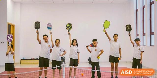 A group of happy students holding paddles for pickleball or similar racket sports, posing together indoors during a P.E. class at Concordia International School Ningbo.